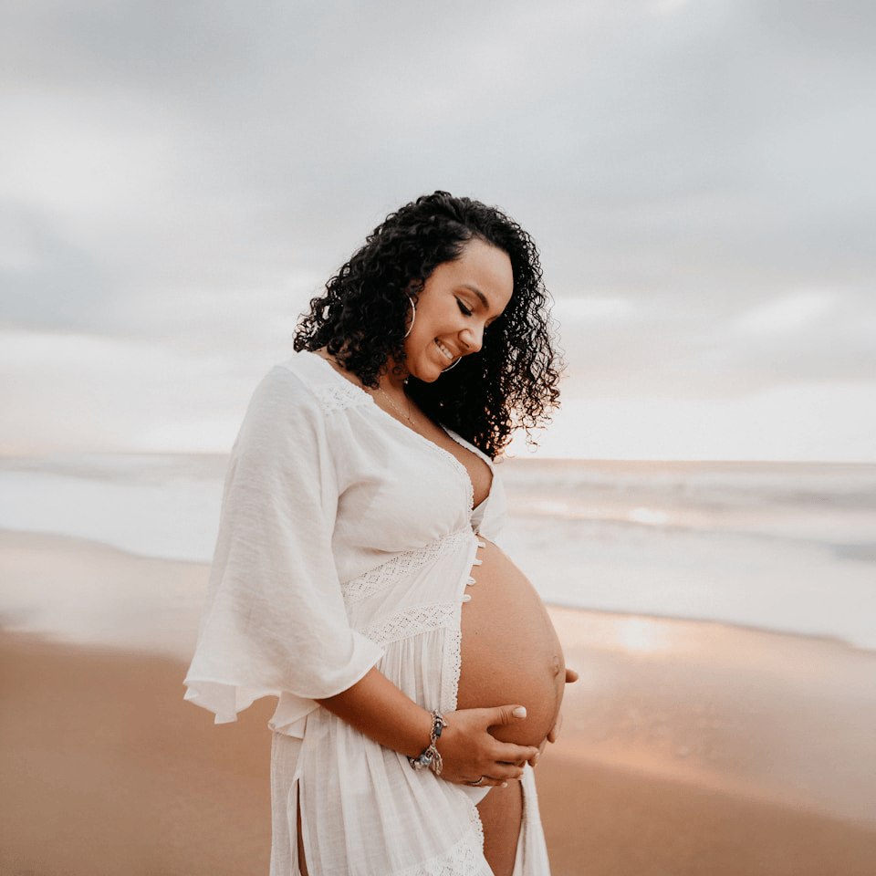 Pregnant mom smiling on a beach. Photo by Vitor Monthay on Unsplash https://unsplash.com/photos/woman-in-white-long-sleeve-shirt-standing-on-beach-during-daytime-R1UkYL5J1r8?utm_source=unsplash&utm_medium=referral&utm_content=creditShareLink